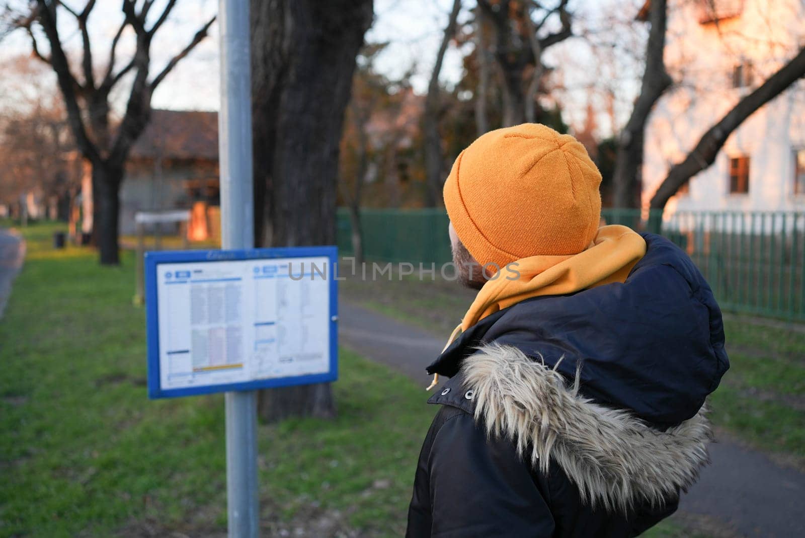Guy in winter coat and yellow hat looking at a bus stop timetable schedule by hotCheeseProductions