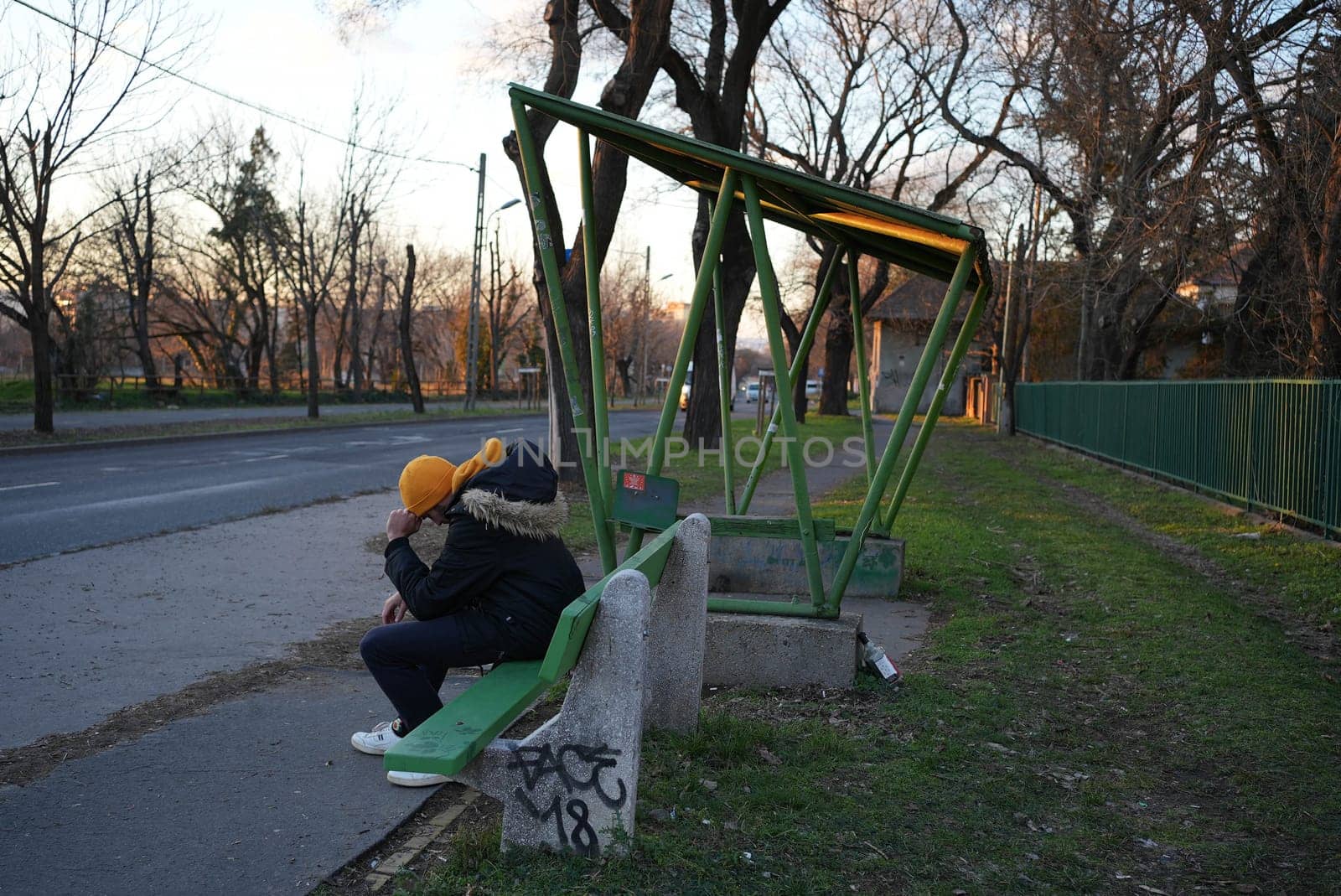 Young man sitting at a bus stop sad holding his head. High quality photo