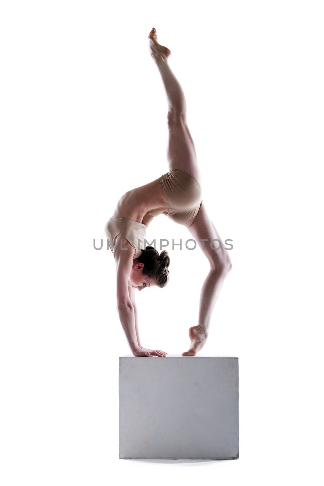 Slim woman balancing on cube in studio, isolated over white background