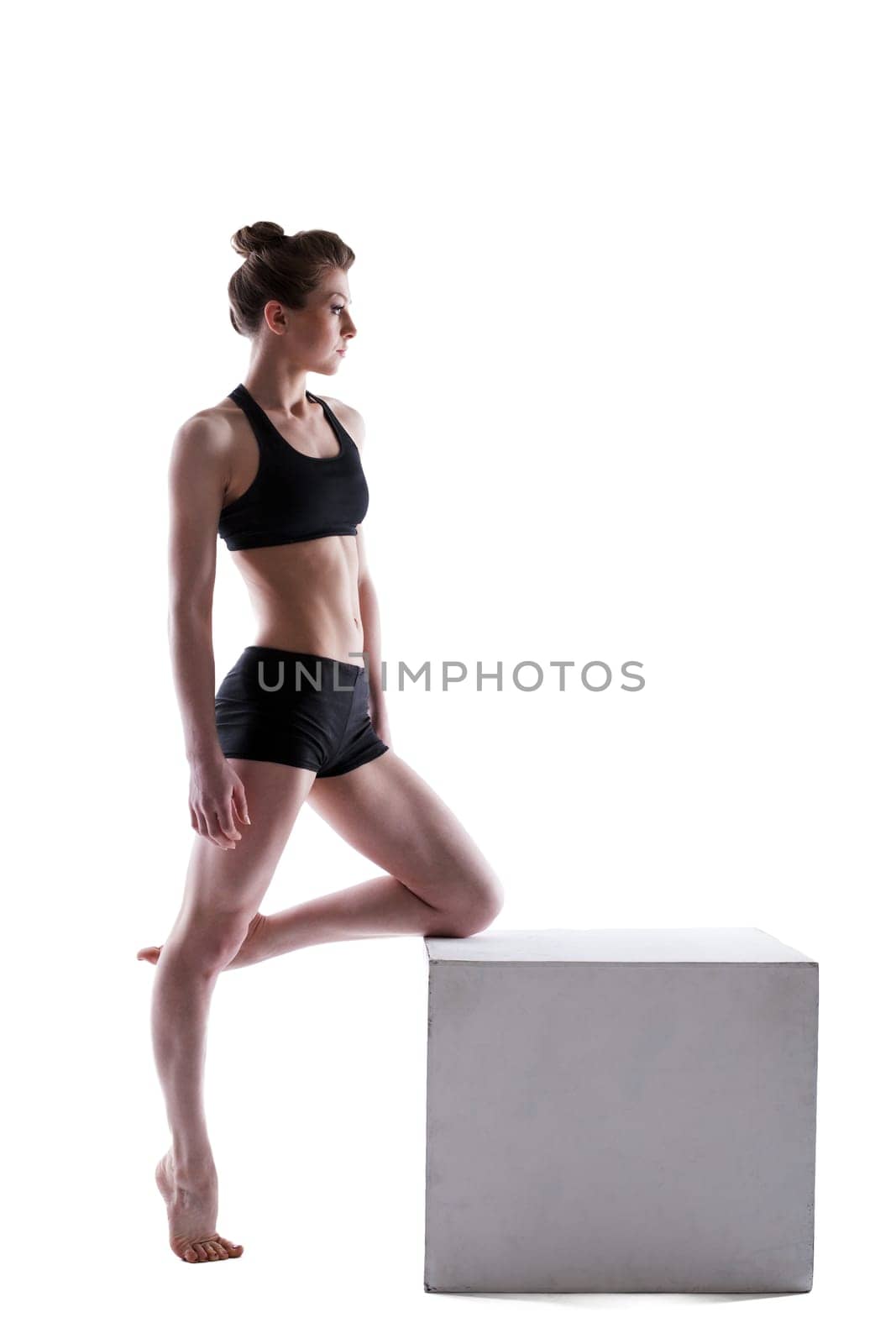 Pretty athletic brunette posing on cube in studio