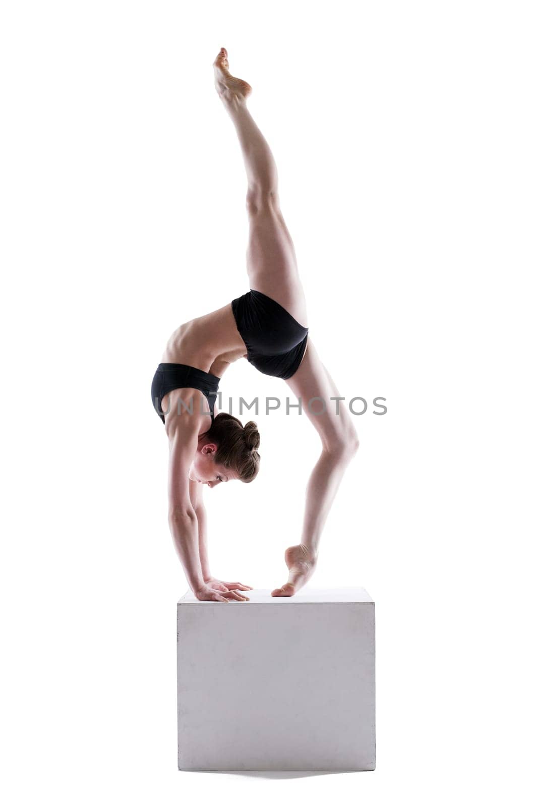 Pretty gymnast posing on cube in studio, isolated over white background