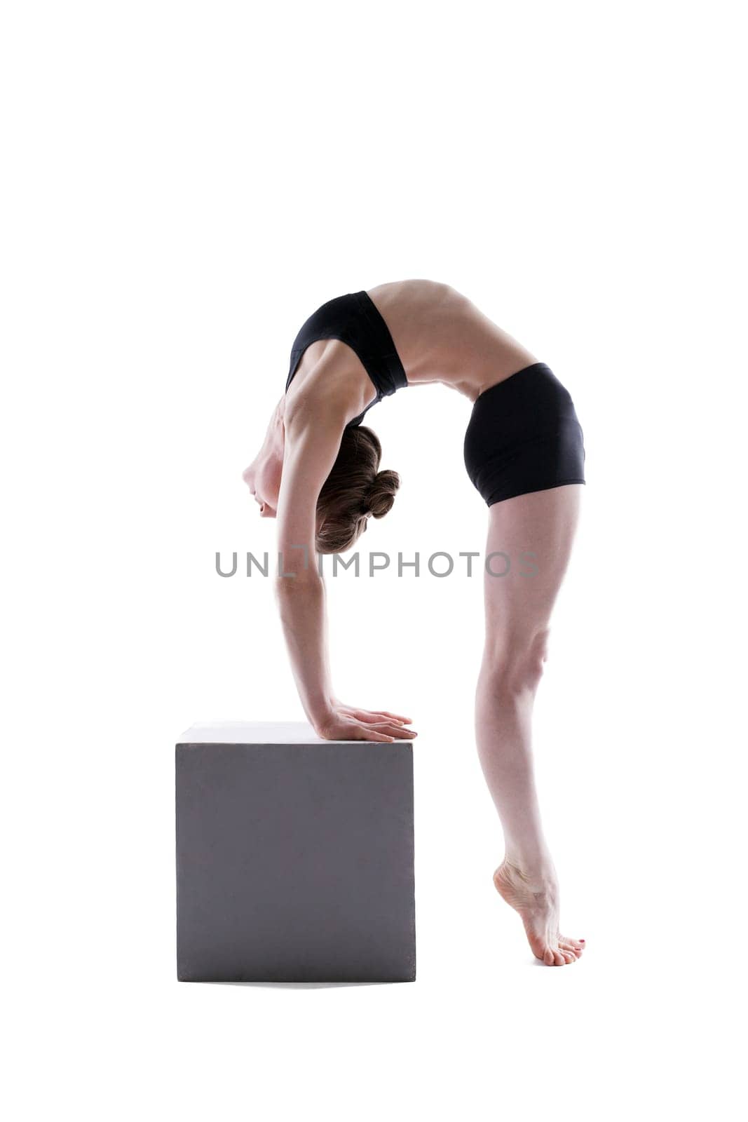 Pretty flexible girl posing on cube in studio, isolated over white background