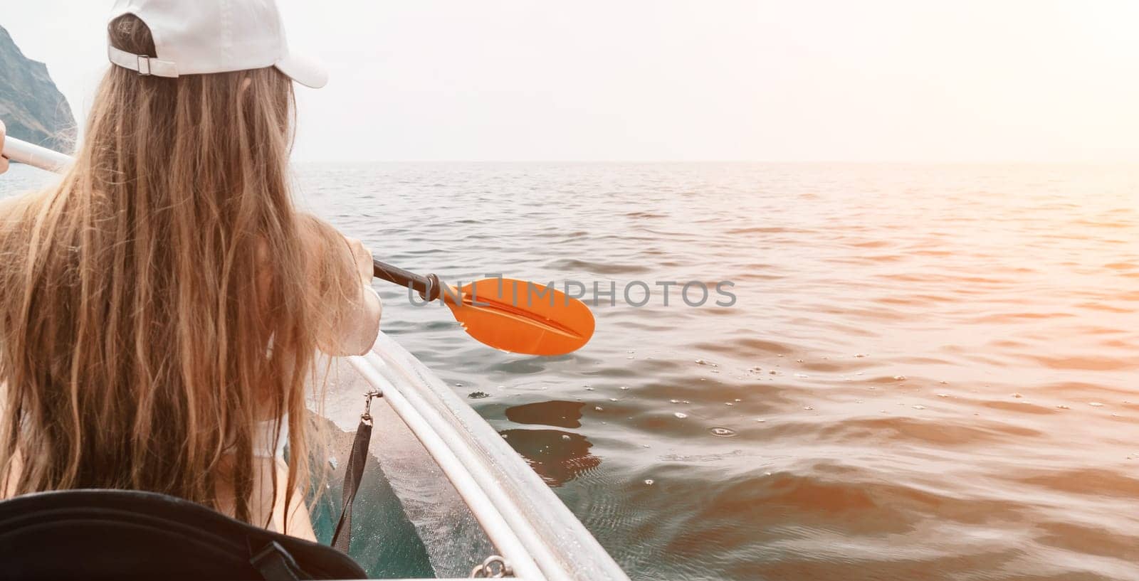 Woman in kayak back view. Happy young woman with long hair floating in transparent kayak on the crystal clear sea. Summer holiday vacation and cheerful female people having fun on the boat.