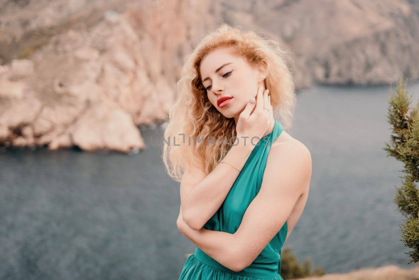 Side view a Young beautiful sensual woman in a mint long dress posing on a volcanic rock high above the sea during sunset. Girl on the nature on overcast sky background. Fashion photo