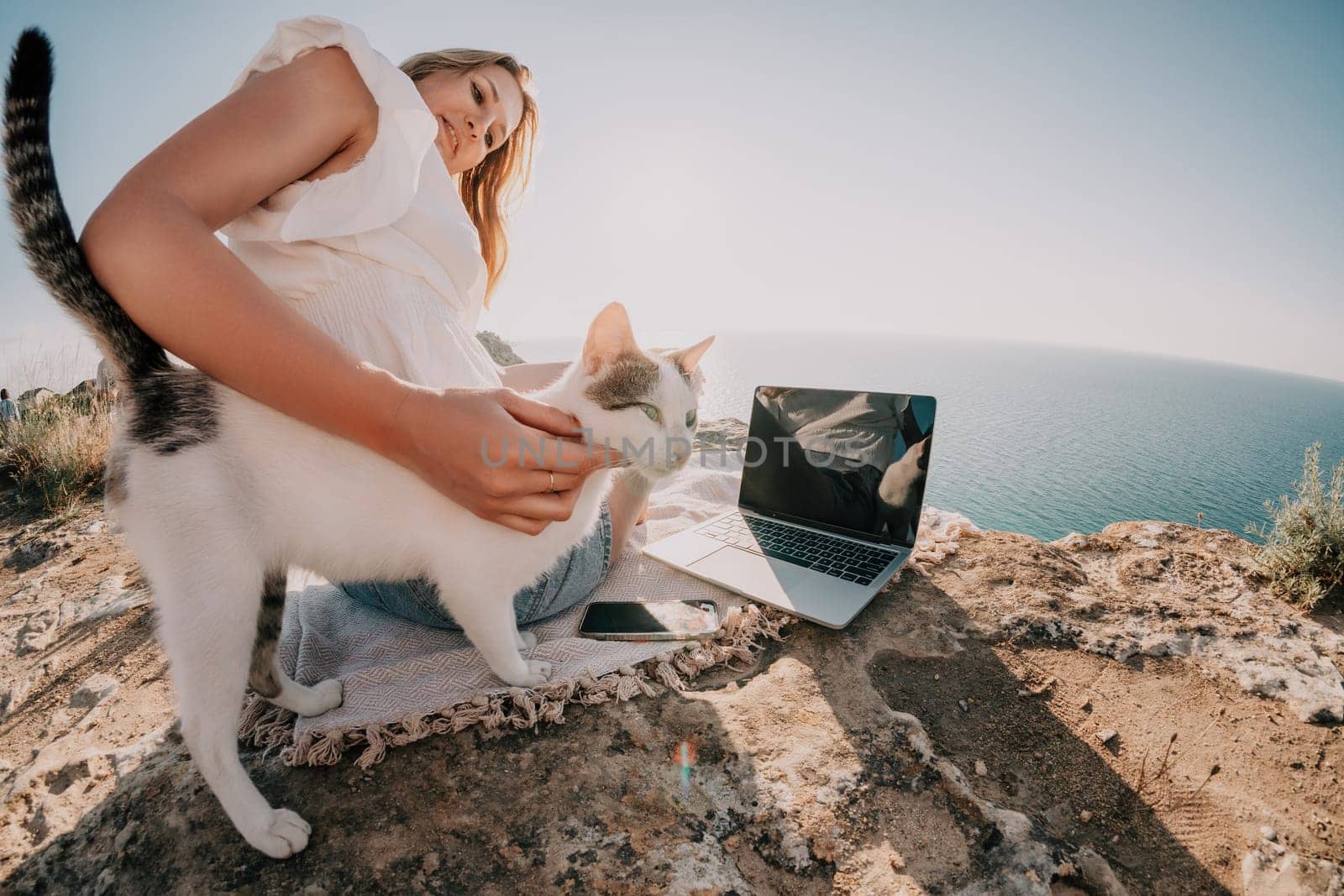 Woman sea laptop. Business woman petting cat and working on laptop by the sea. Close up on hands of pretty lady typing on computer outdoors summer day. Freelance, digital nomad and holidays concept. by panophotograph