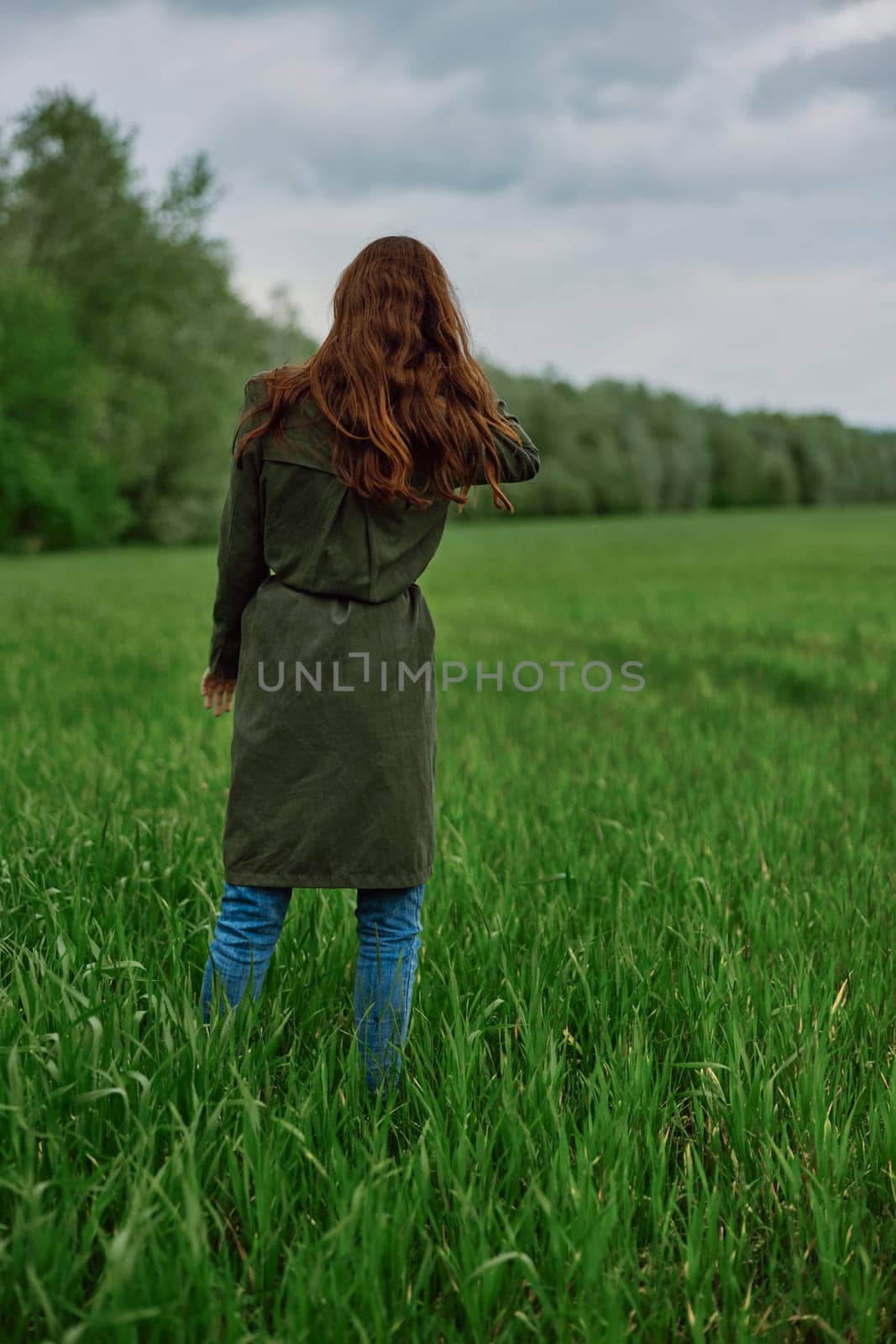 a woman with long red hair stands with her back to the camera in a field in tall green grass by Vichizh