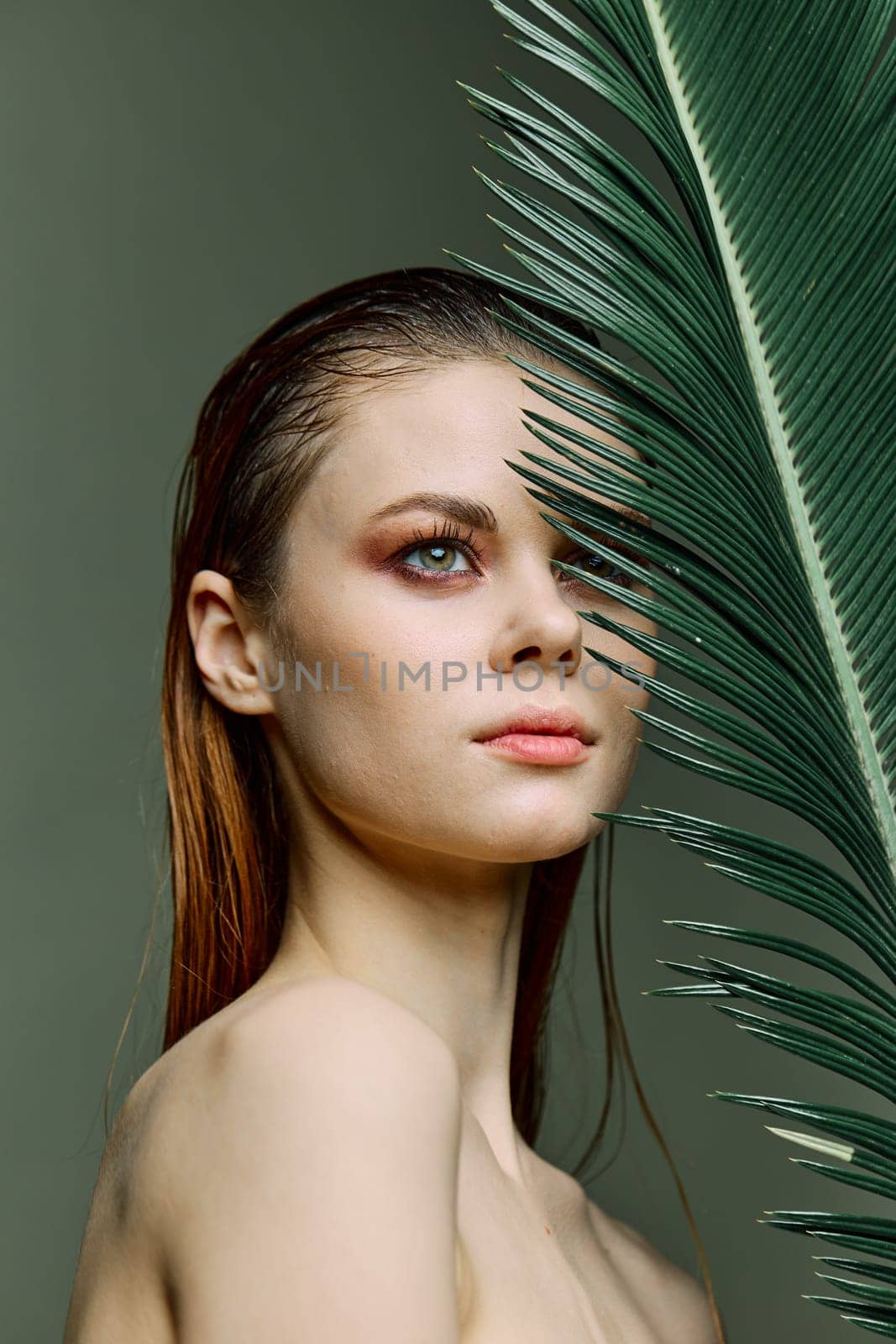 beauty portrait of a beautiful, elegant woman standing holding a palm leaf near her face, looking away. Vertical photo without retouching of problem skin by Vichizh