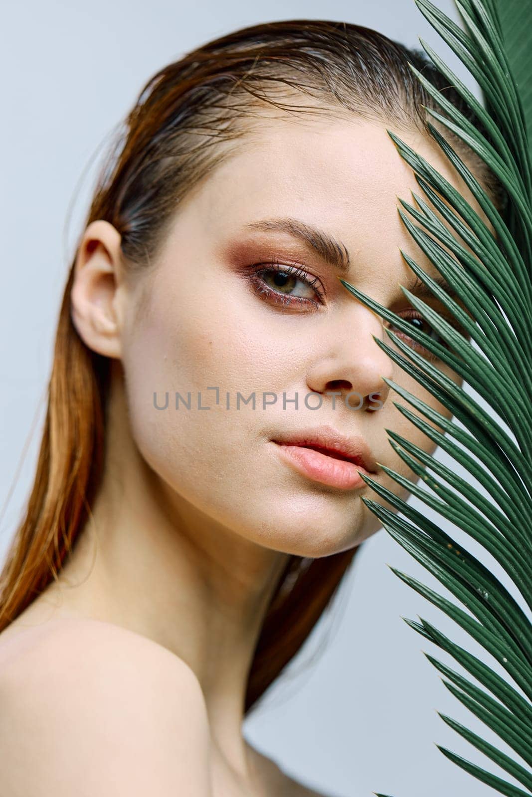 a close beauty portrait of a beautiful woman standing holding a tropical palm leaf in her hand, bringing it to her face. Vertical photo without retouching. High quality photo