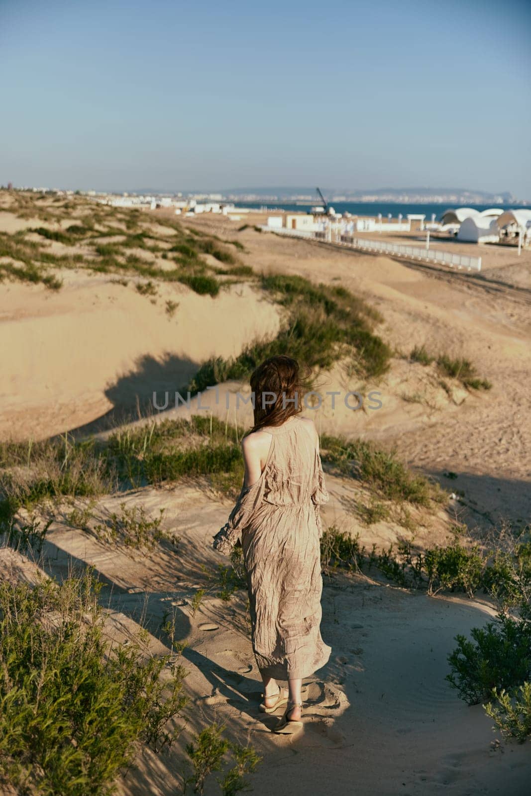 a woman walks on the sand away from the sea in windy weather enjoying the pleasant weather with her back to the camera. High quality photo