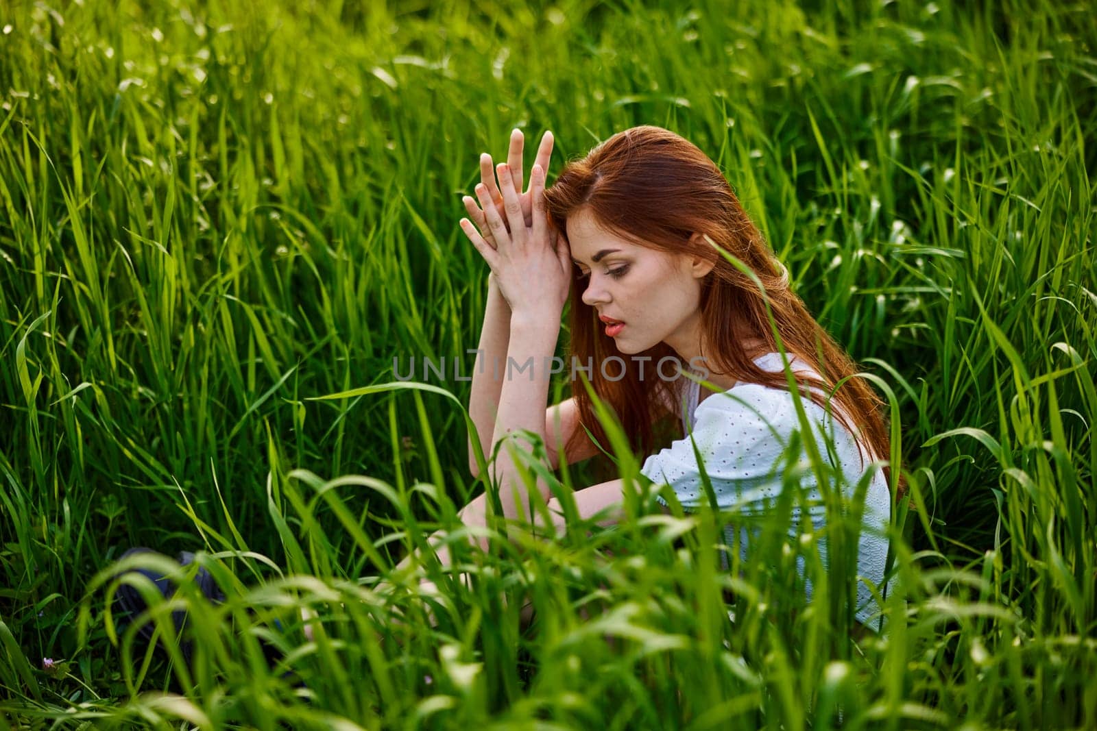sad woman sitting in tall green grass on a sunny day. High quality photo