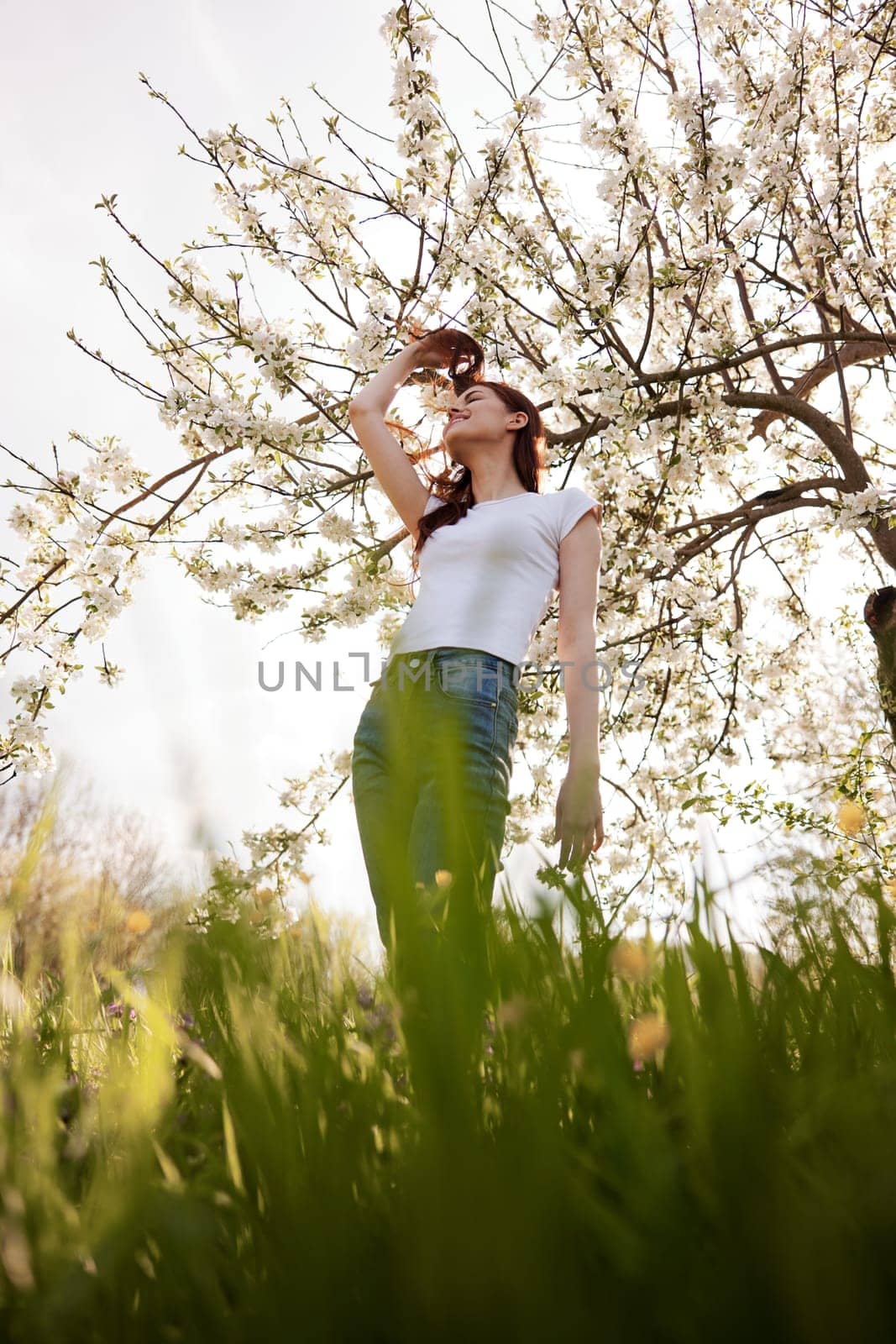joyful woman stands against the background of a flowering tree in summer clothes by Vichizh