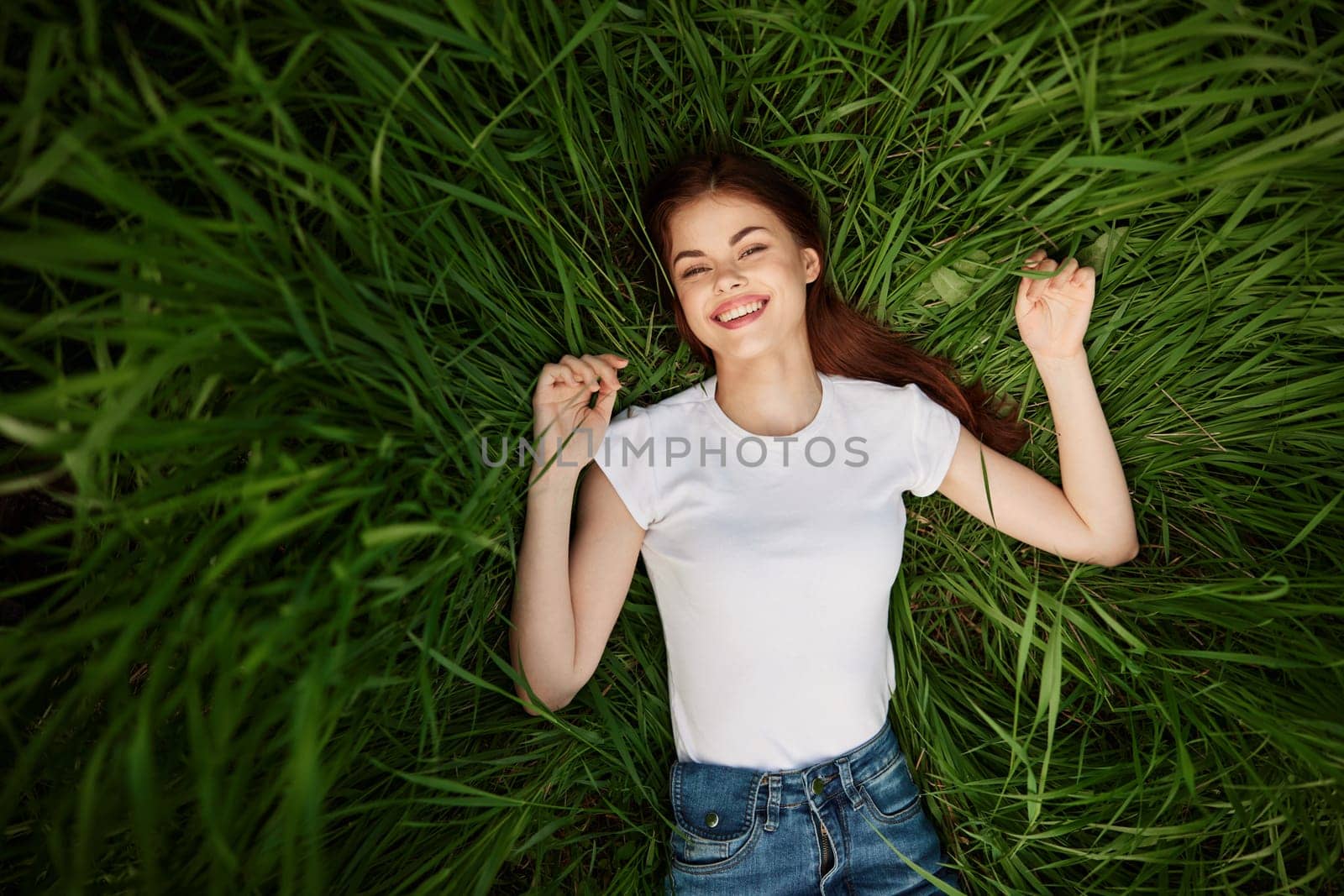 a woman with even, white teeth laughs in the green grass. High quality photo