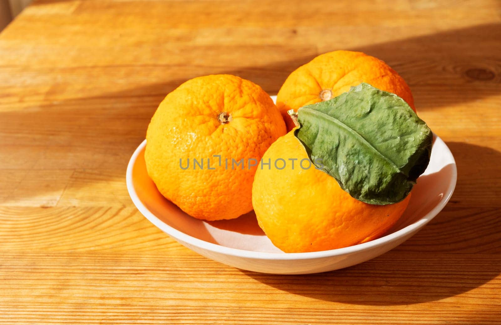 Oranges in white plate on wooden table , fresh fruit with green leaves , healthy eating