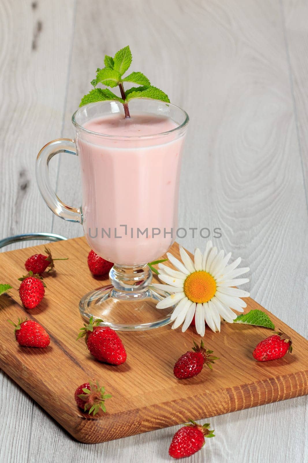 Glass of delicious milk shake with mint and fresh strawberries, chamomile on wood cutting board