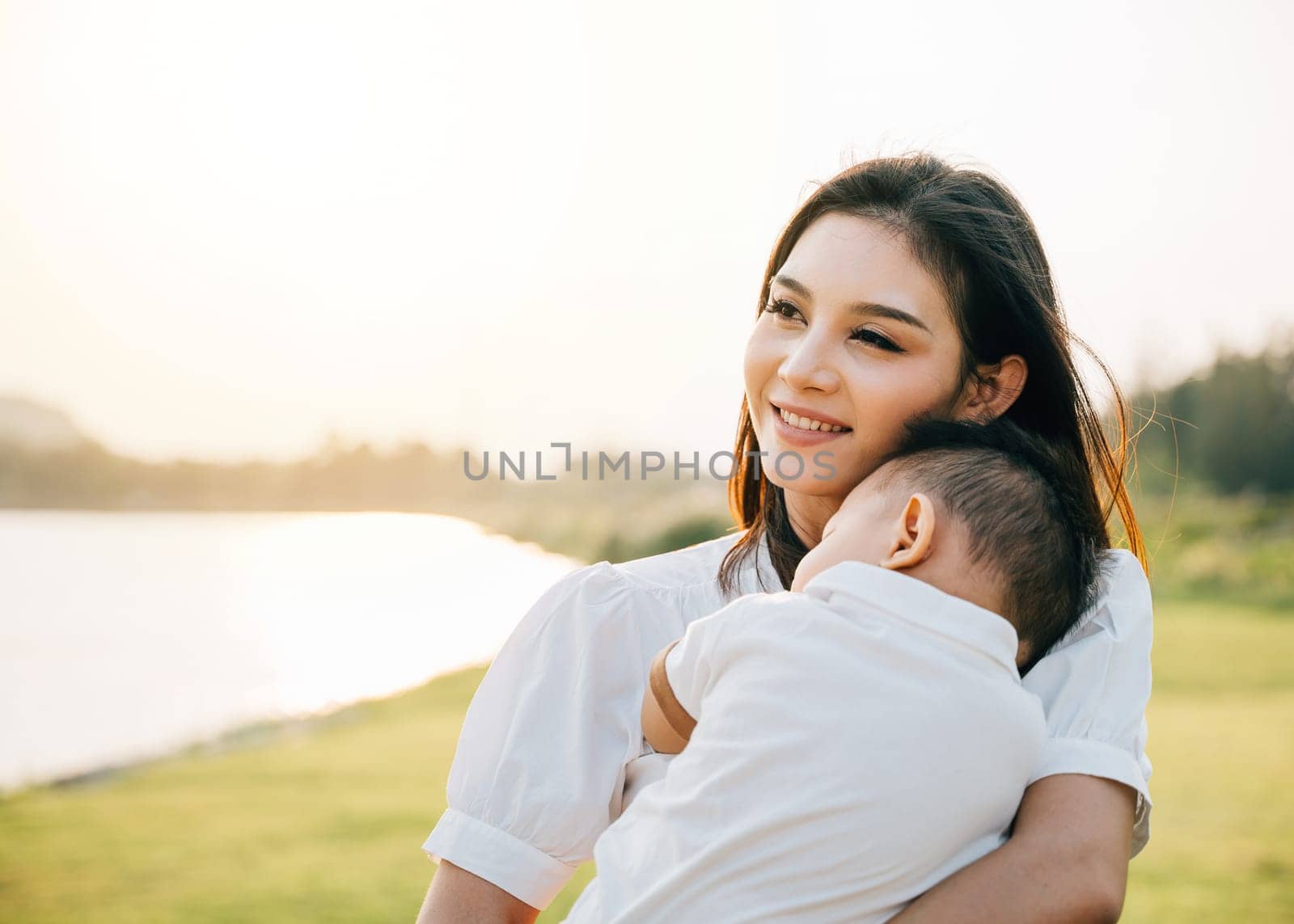 Happy beautiful mother holding baby sleeping son in the park by Sorapop