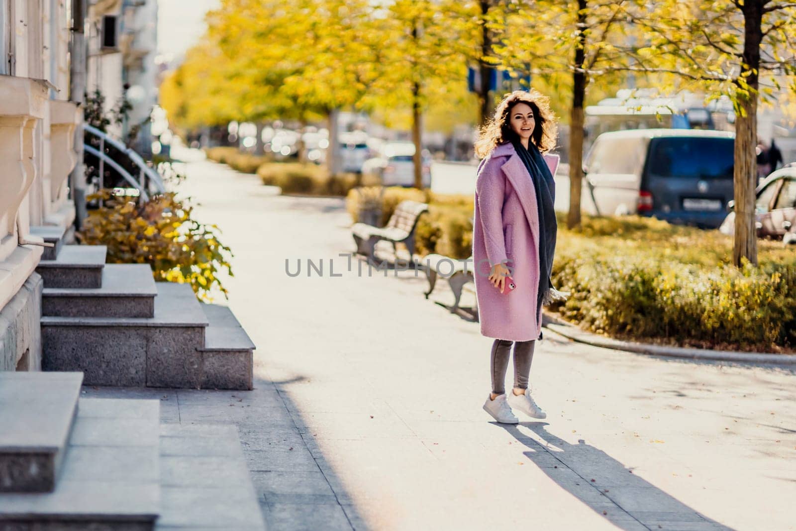 Woman autumn city. A woman in a pink faux fur coat posing on a city street in autumn on a sunny day. Trees with yellow foliage along the street