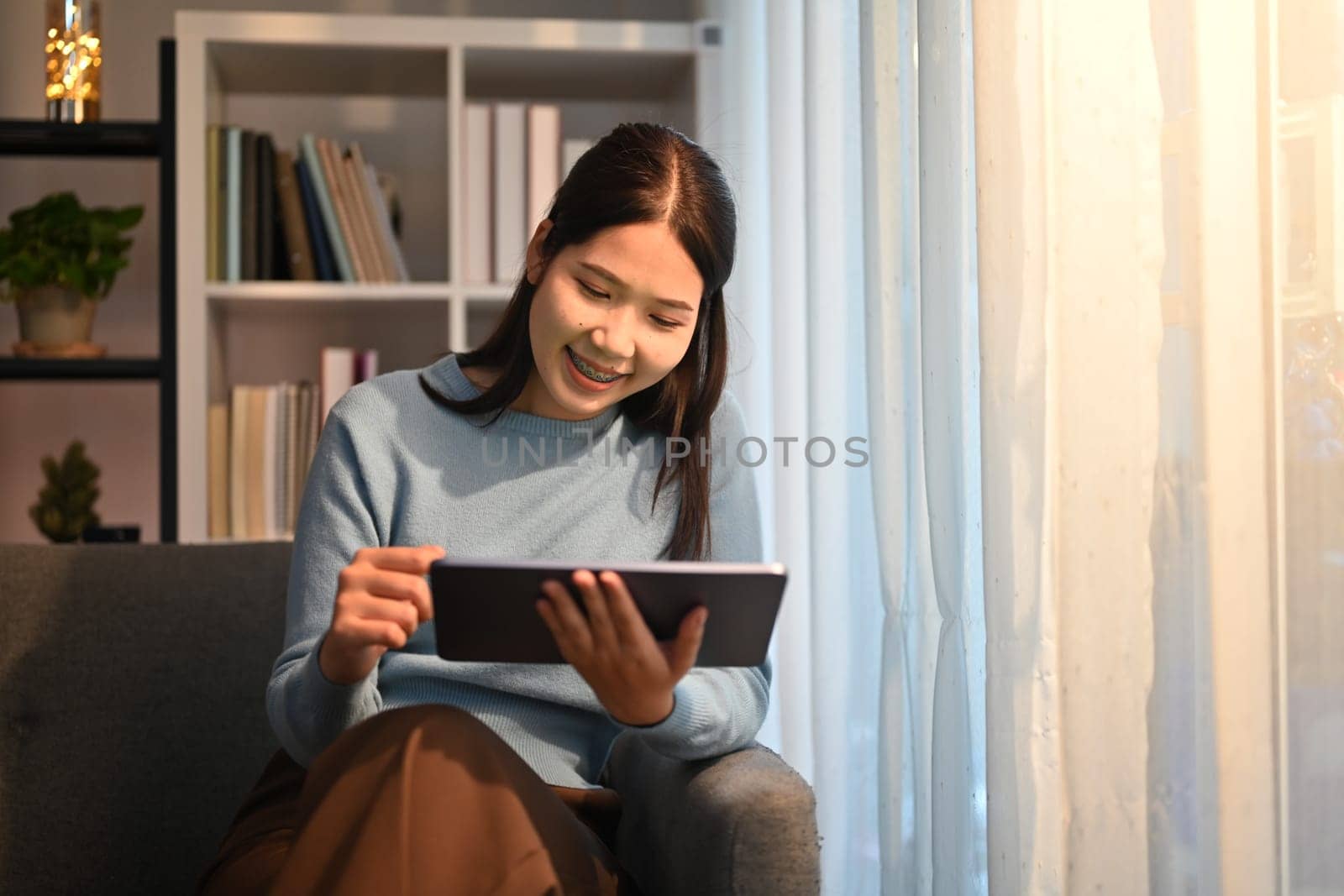 Pleasant millennial woman reading email or checking daily routine on digital tablet, sitting in living room.