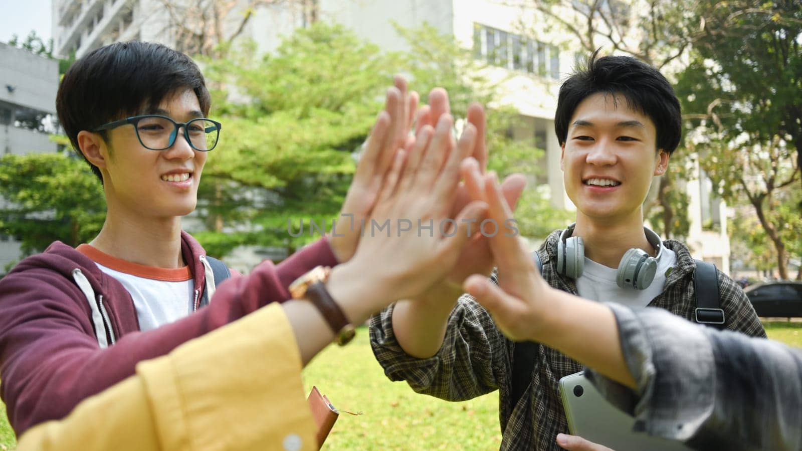 Group of university friends giving high five, celebrating together. University, youth lifestyle and friendship concept.