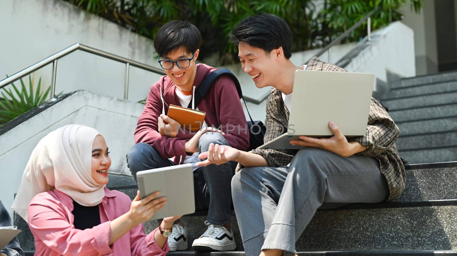 Happy students are sitting on college stairs and discussing their home assignment. Youth lifestyle and education concept.