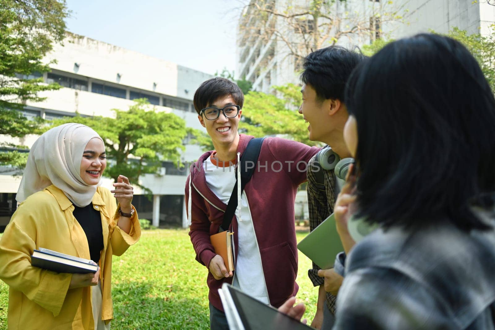 Multiethnic group of cheerful university student talking to each other after classes while walking in campus outdoors.
