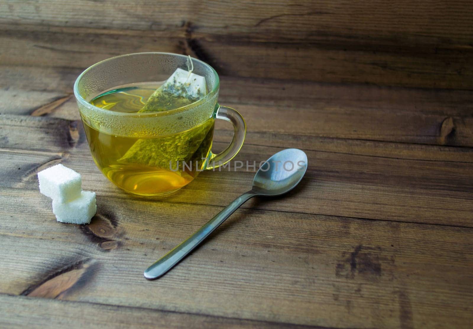 Green tea in a glass mug, sugar and a spoon. Green tea in a glass mug, sugar and a spoon on a wooden table.