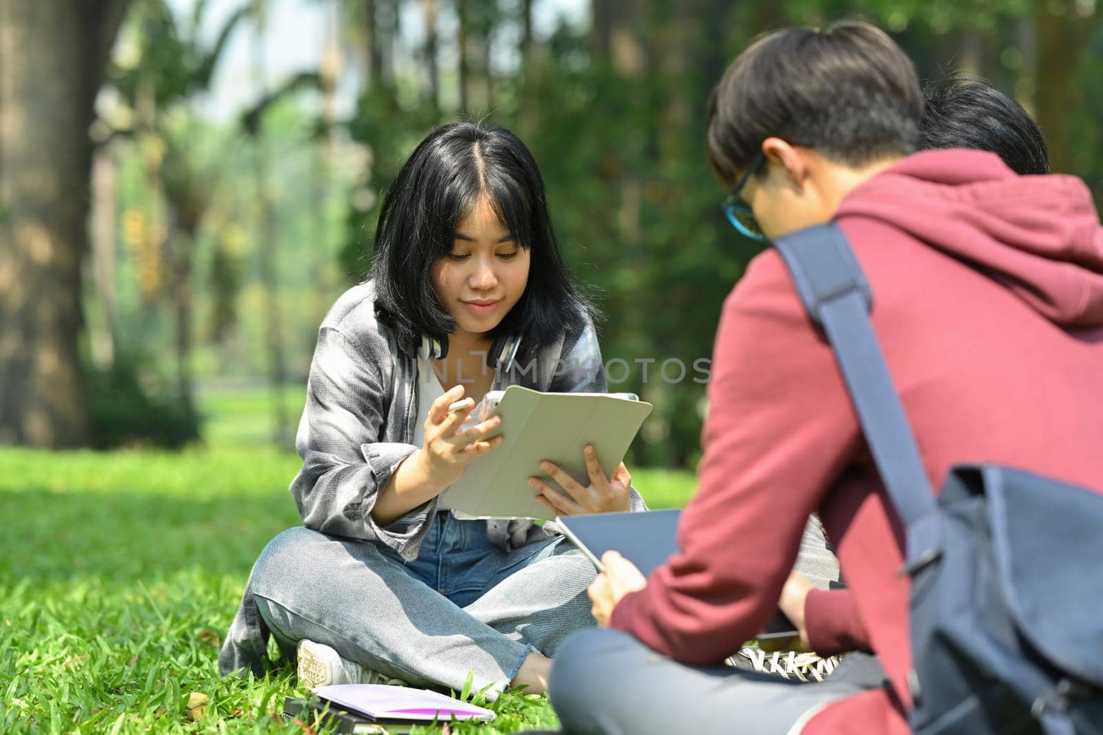 Image of asian female student reading books with her friends at summer park. Education and lifestyle concept by prathanchorruangsak