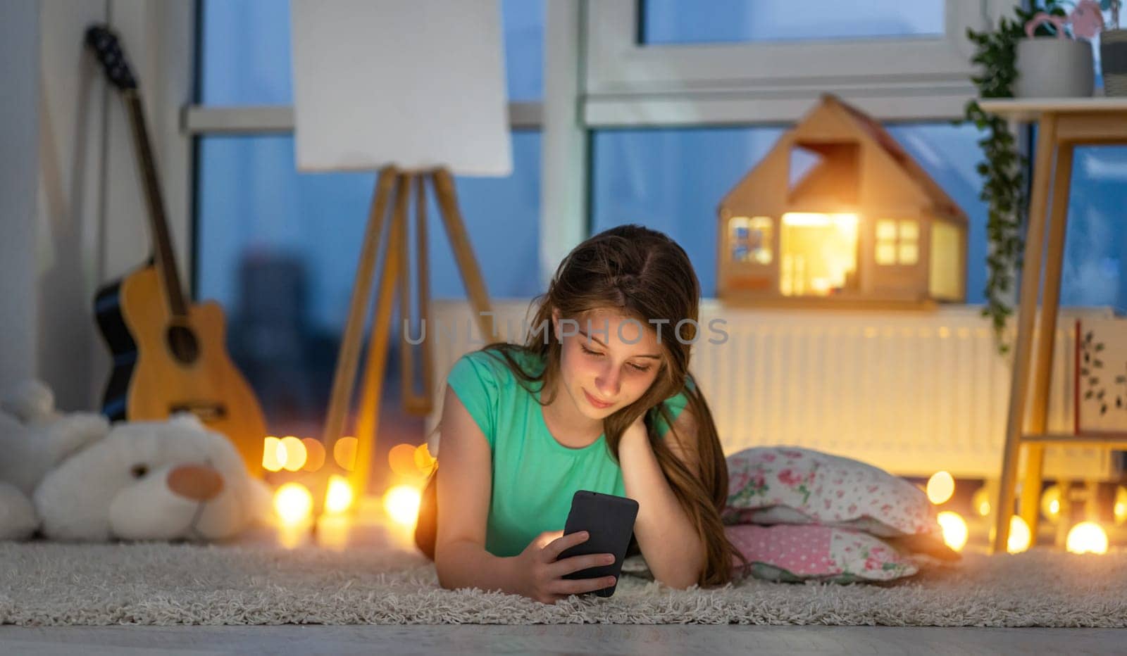 Young girl lying on floor in evening room with smart phone