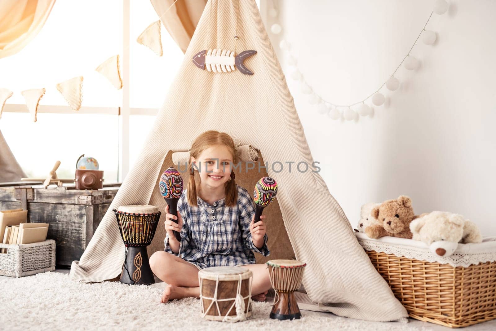 Little girl playing in room with maracas and djembe drums in kids wigwam