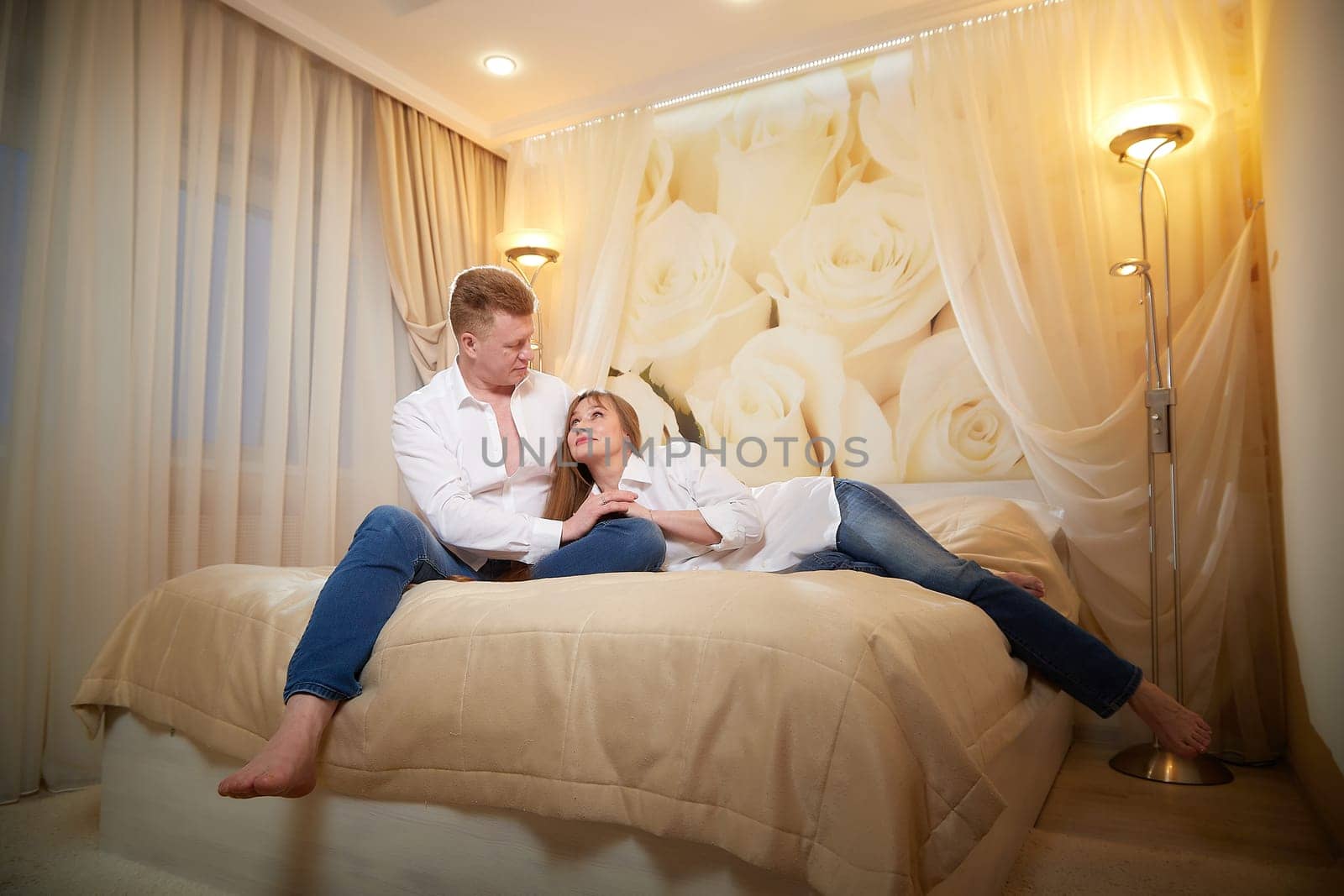 An adult couple of newlyweds in in white shirts in a hotel room after the wedding. A guy and a girl, a man and a woman in a beautiful room. The concept of love and care by keleny