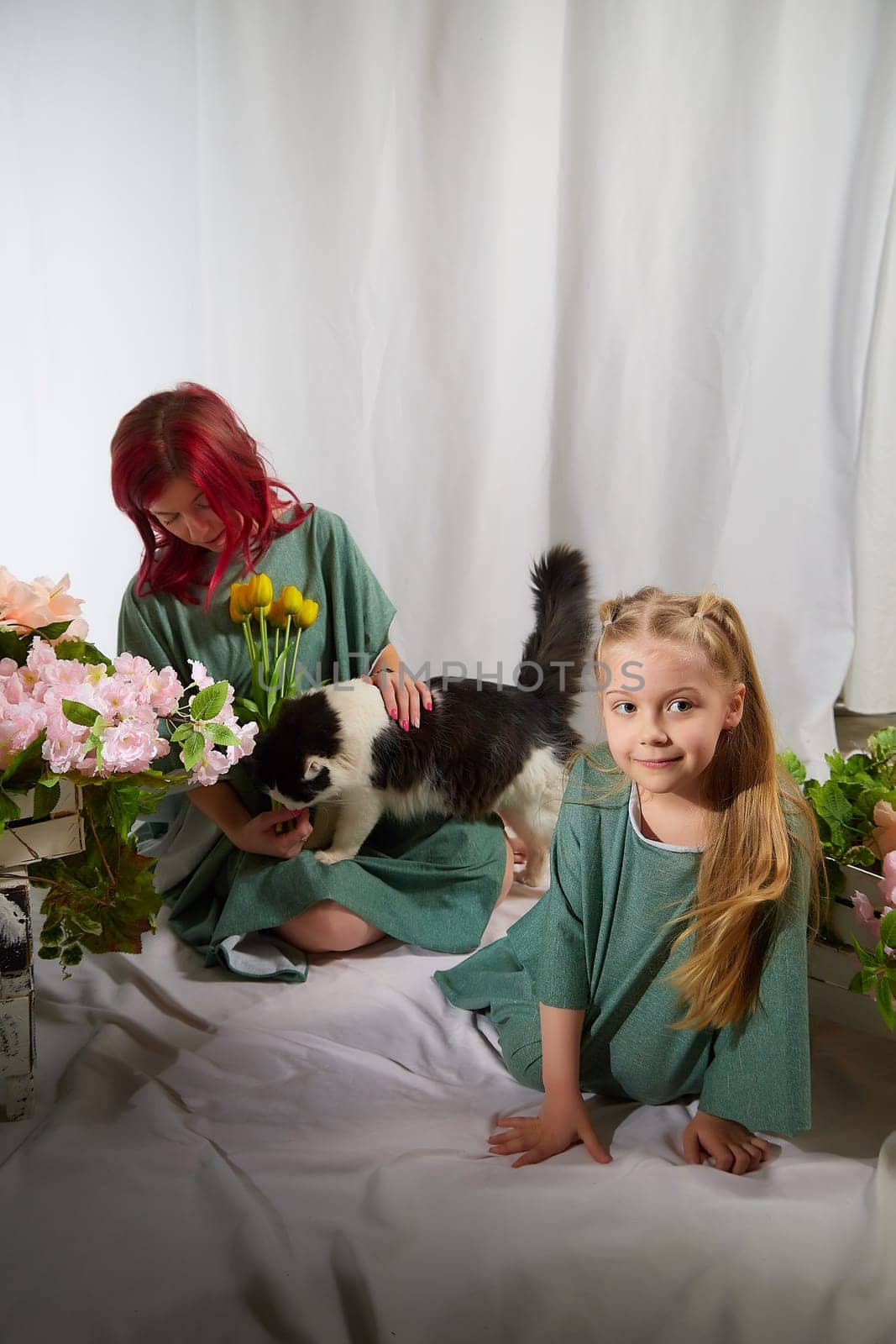 Amazing pretty mother and daughter having fun with flowers and cat in 8 March or in Mother's day. Red haired mom and small little blonde girl having lovely free time on white background with pet by keleny