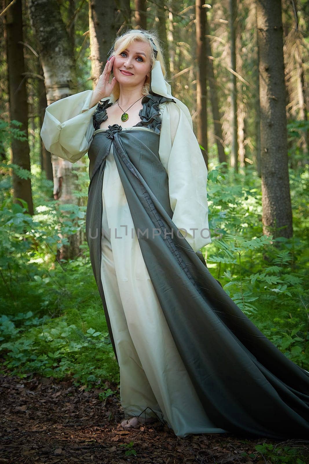 Adult mature woman 40-60 in a green long fairy dress in forest. Photo shoot in style of dryad and queen of nature. Fairy in beautiful green summer forest. Concept of caring for nature