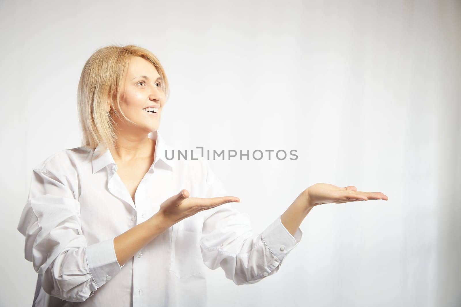 Portrait of a pretty blonde smiling woman posing on white background and pointing somewhere. Happy girl model in white shirt posing in studio. Copy space