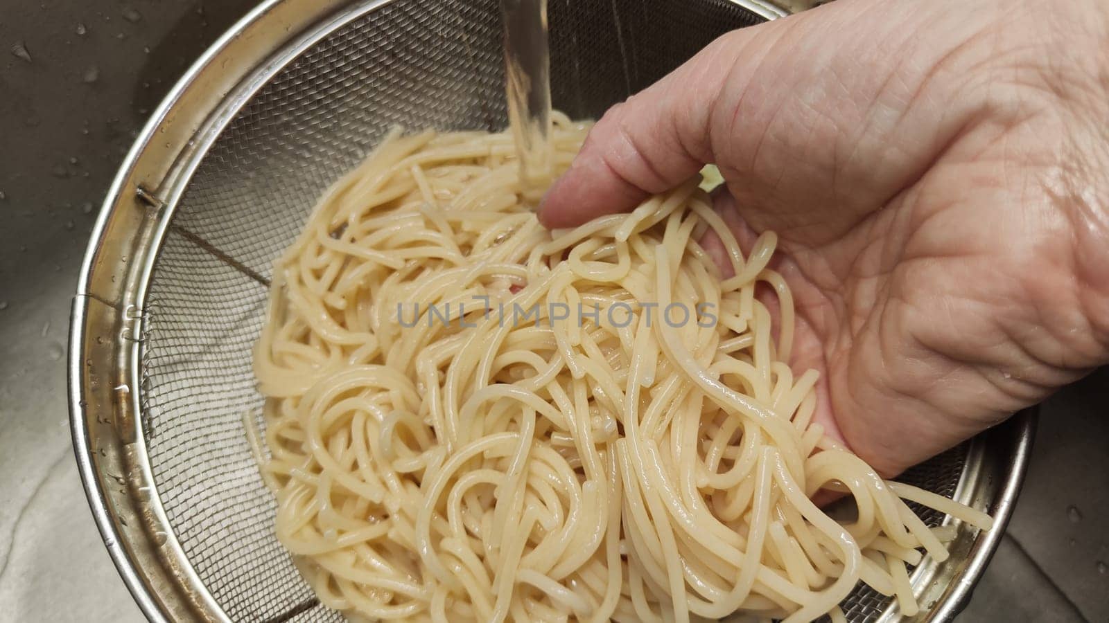 Yellow white thin strands of noodles in the metal bowl. Raw and uncooked. Cooking noodles in boiling water and rinsing vermicelli or spaghetti with water by woman hand