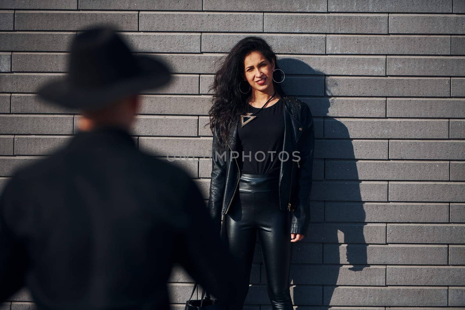 Beautiful couple in black clothes together against wall outdoors.