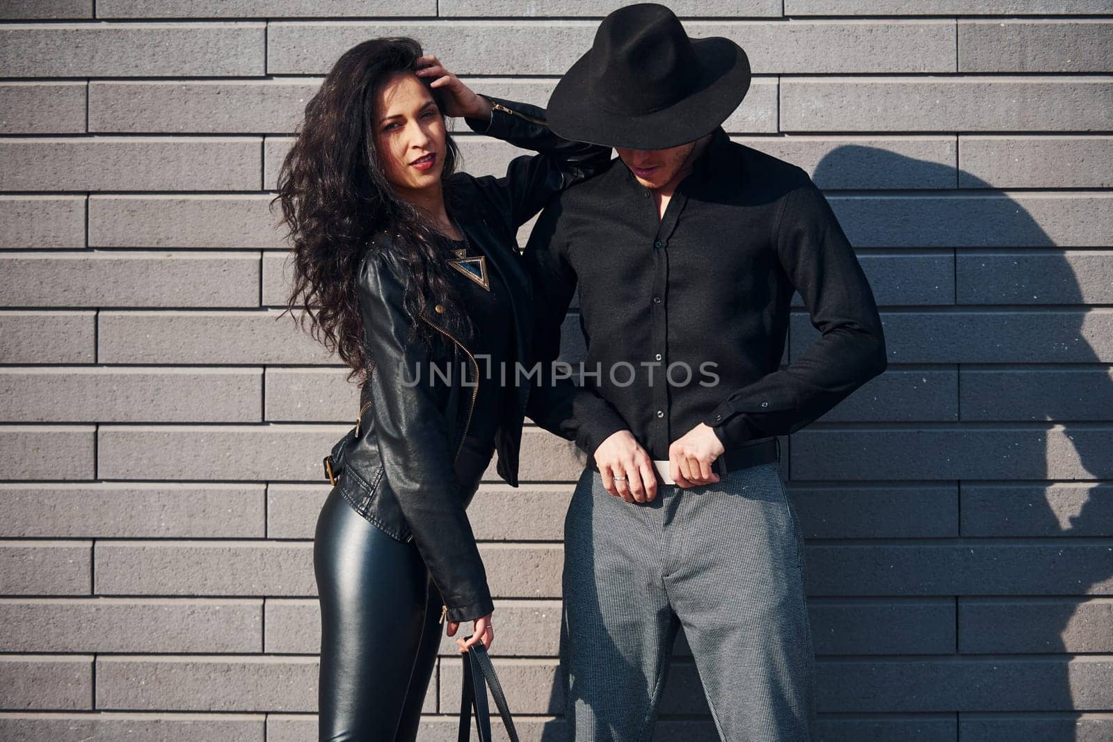 Beautiful couple in black clothes together against wall outdoors by Standret