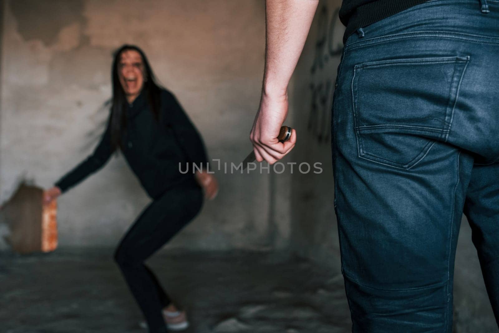 Rear view of psycho with knife that follow young girl in abandoned building by Standret