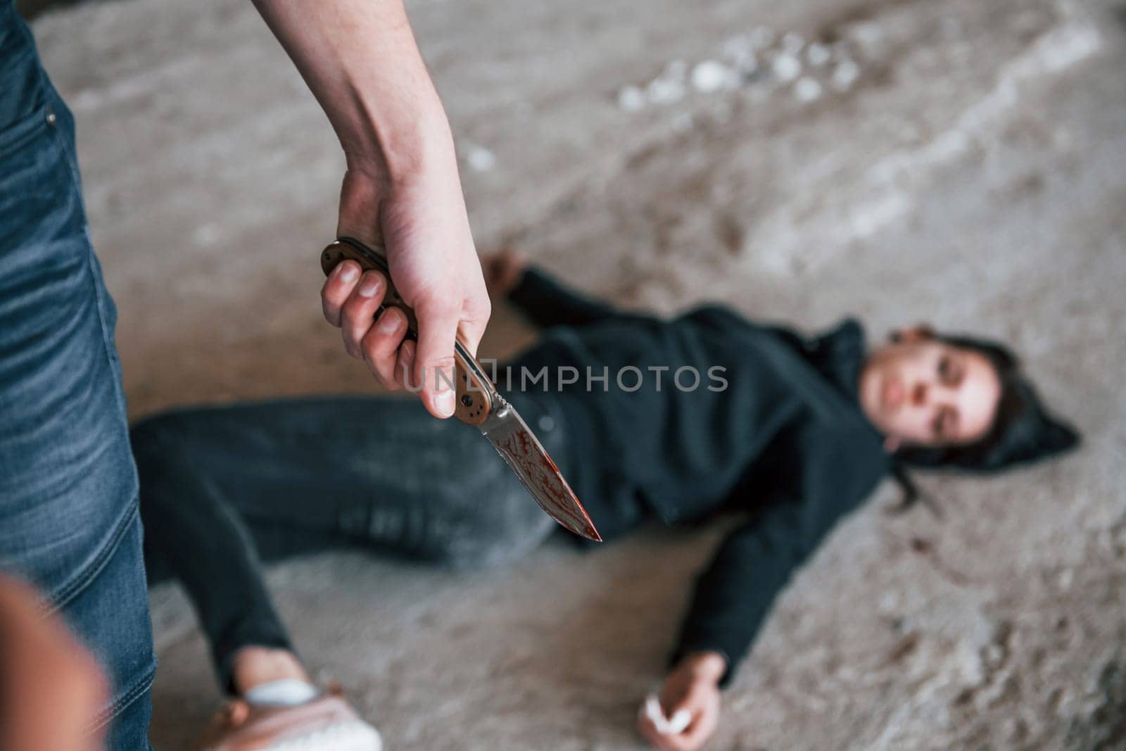 Murderer with knife covered in blood standing near his dead female young victim.