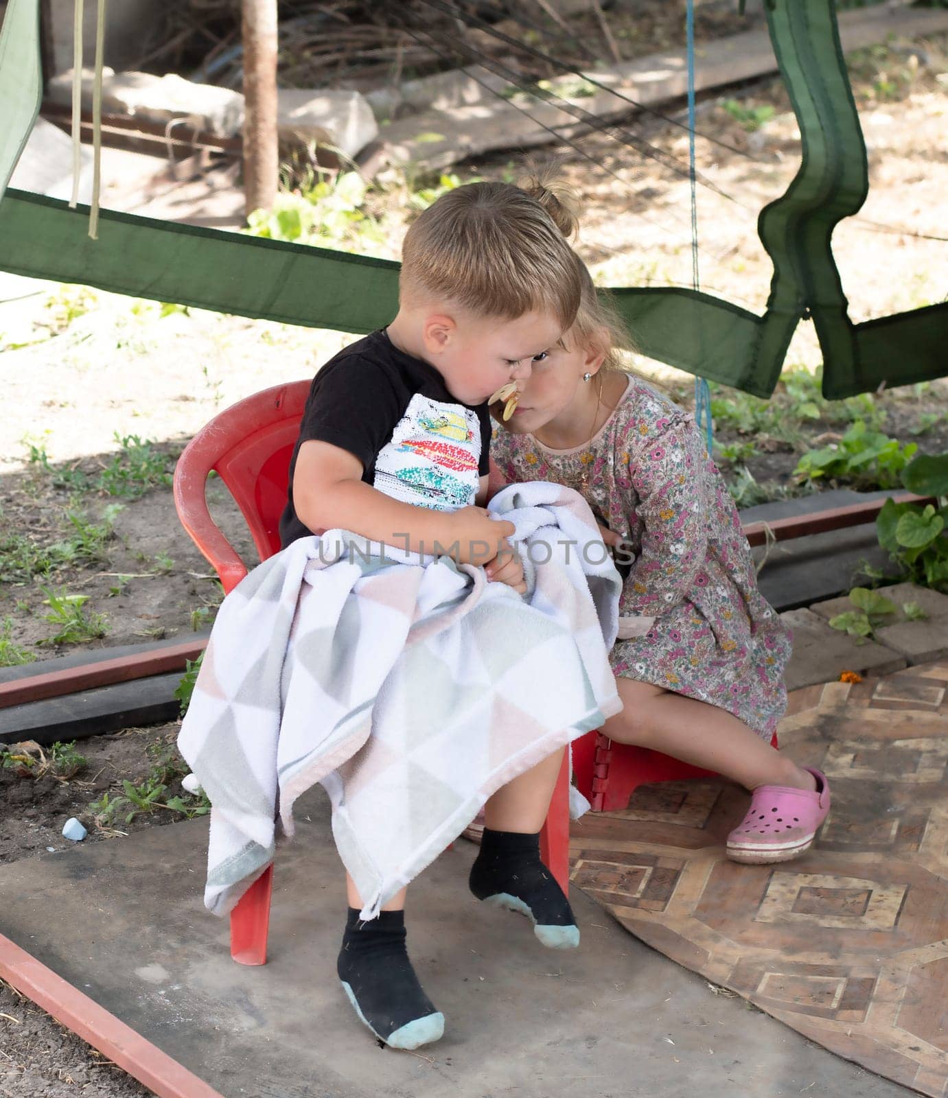 Two small children, a bright boy and a girl, sit on a high chair outside and hug each other in the summer cottage. Children are smeared, dirty and soiled.
