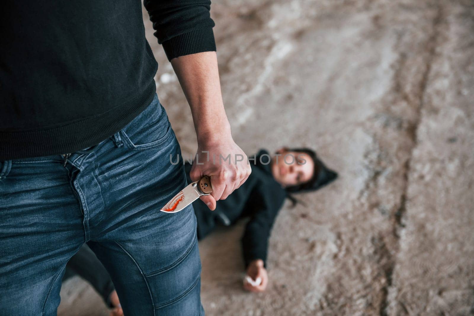 Murderer with knife covered in blood standing near his dead female young victim.