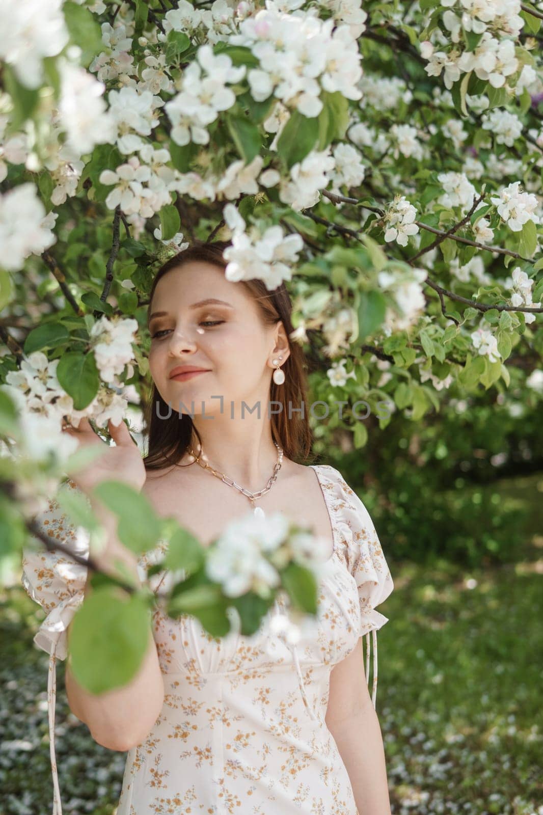 An attractive long-haired woman walks in the spring in the park of blooming apple trees. Spring portrait of a woman