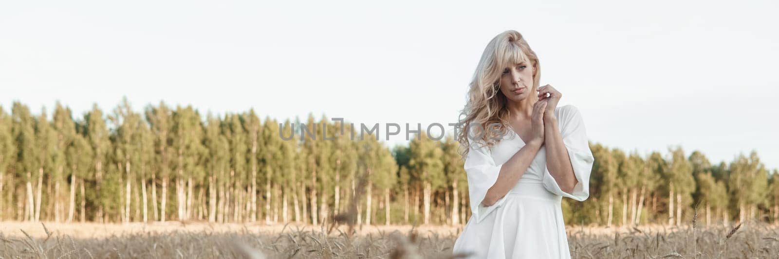 A blonde woman in a long white dress walks in a wheat field. The concept of a wedding and walking in nature. by Annu1tochka