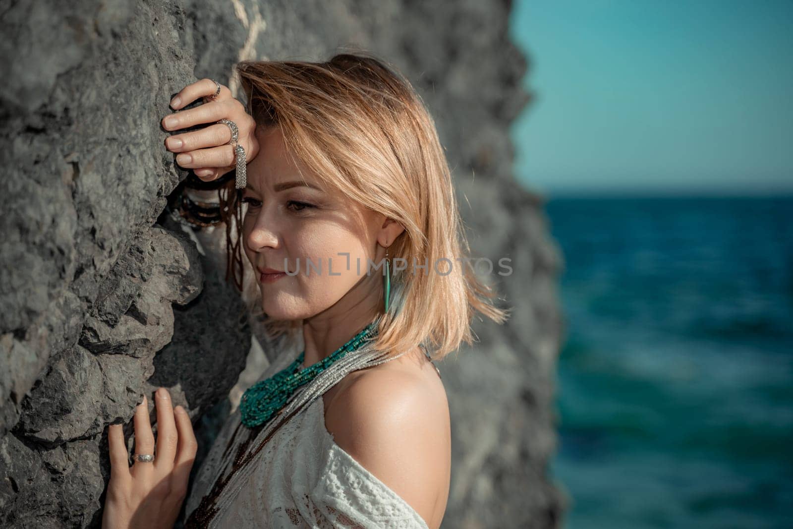 Middle aged woman looks good with blond hair, boho style in white long dress on the beach decorations on her neck and arms