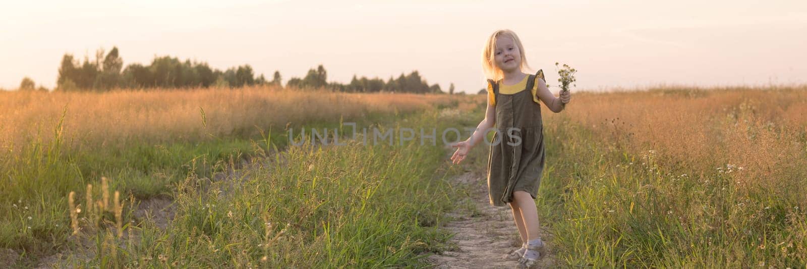 A little blonde girl is sitting walking on a chamomile field and collecting a bouquet of flowers. The concept of walking in nature, freedom and a clean lifestyle