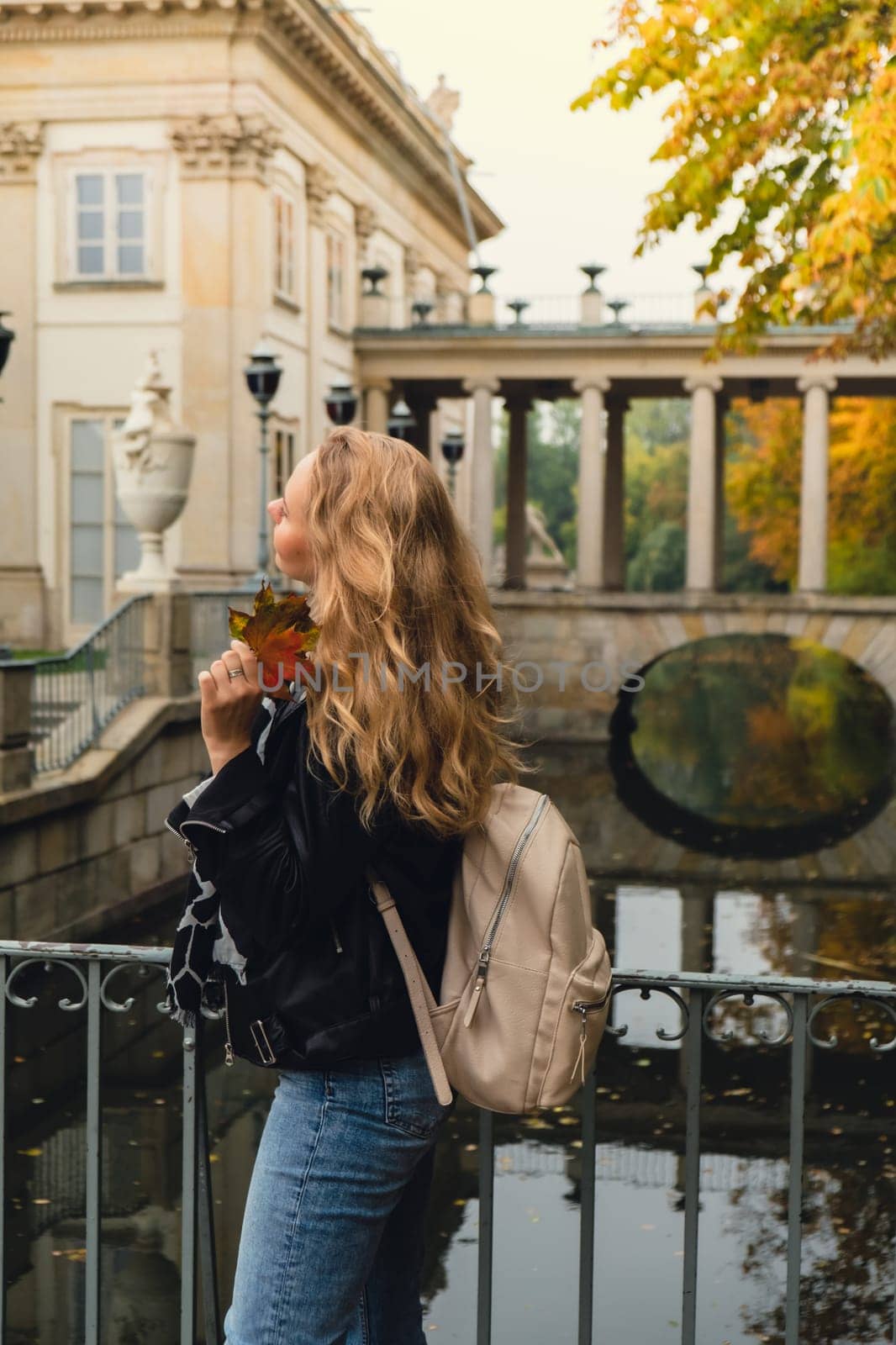 Tourist attraction woman travel enjoying nature sightseeing Baths classicist Palace on the Isle in Lazienki Park touristic place in Warsaw. Lazienki Royal Baths Park, Warsaw Poland. Colorful Autumn Foliage and Mirror Reflection on the Lake. Yellow leaves Nature in autumn Baroque columns