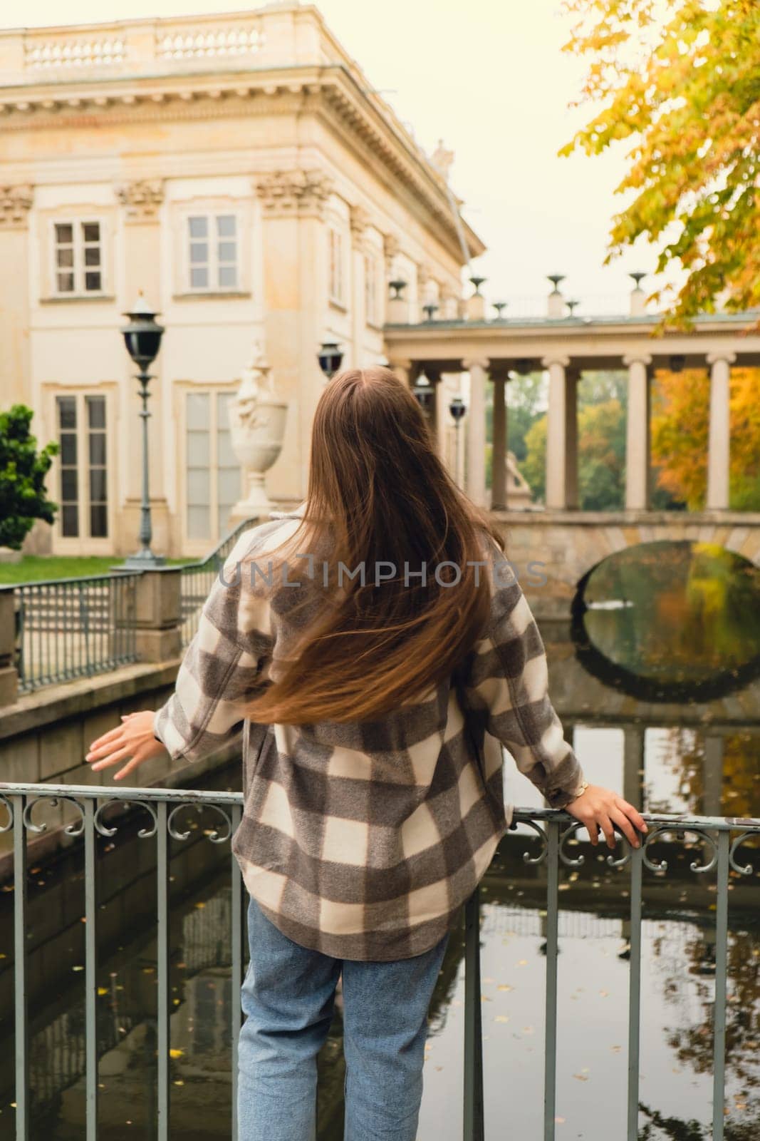 Tourist attraction woman travel enjoying nature sightseeing Baths classicist Palace on the Isle in Lazienki Park touristic place in Warsaw. Lazienki Royal Baths Park, Warsaw Poland. Colorful Autumn Foliage and Mirror Reflection on the Lake. Yellow leaves Nature in autumn Baroque columns