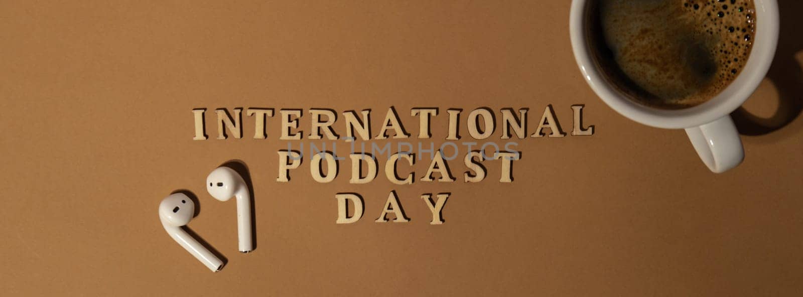 Announcement text INTERNATIONAL PODCAST DAY on beige background with white cup of coffee wireless headphones. Podcasting concept. Listening radio audio healing wellness sound health habits