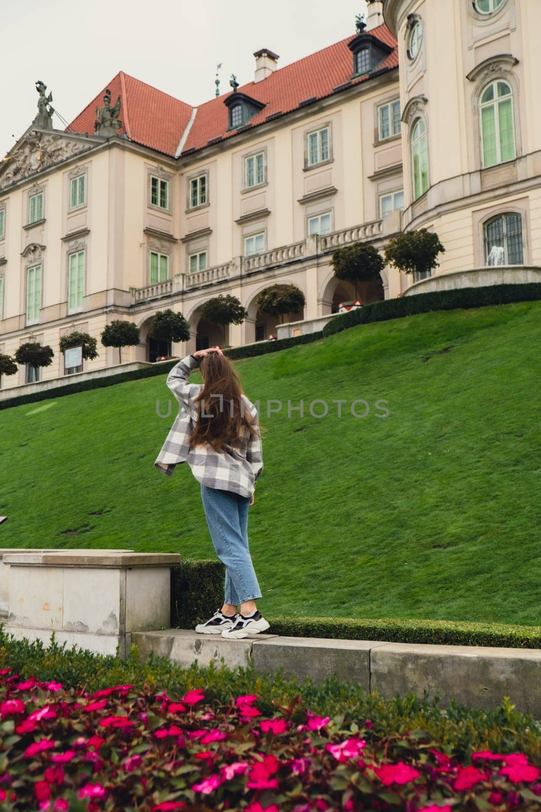 Female woman traveler sightseeing vacation holiday concept Beautiful violet flowers Castle Gardens on background adjacent to the Royal Castle in Warsaw from the side of the Vistula. City landmarks. Tourist attraction