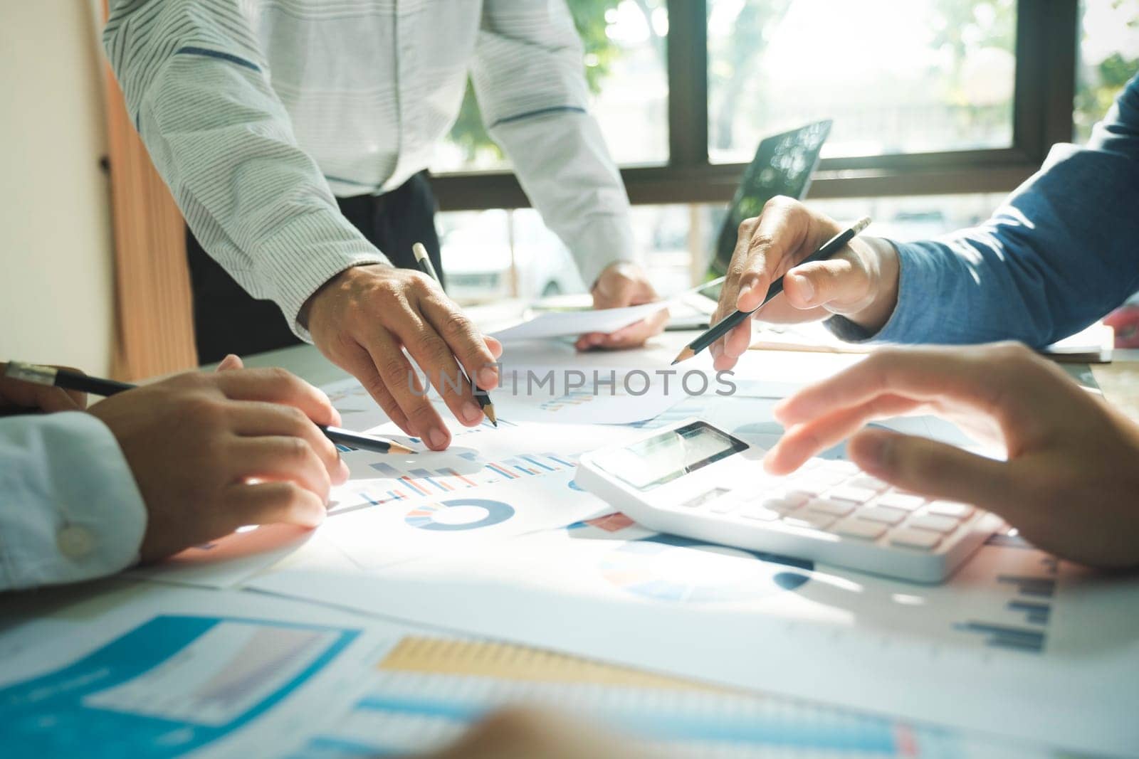 Close-up of businessmen working together at workplace, discussing about strategies, plans, analytic progress, and financial stats, and pointing at graph documents on desk holding pencils and calculator. Business and Teamwork concept.