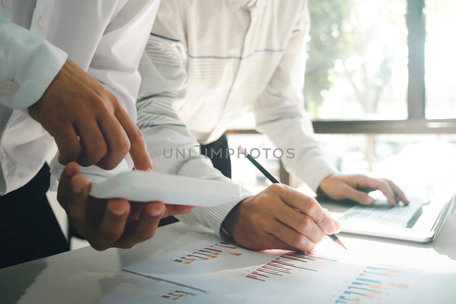 Close-up of businessmen working, meeting together at desk in workplace, office using laptop, holding pencils and pointing at graph documents and calculator for discussing about strategies, plans, analytic progress, and financial stats of company. Business, Teamwork concept.