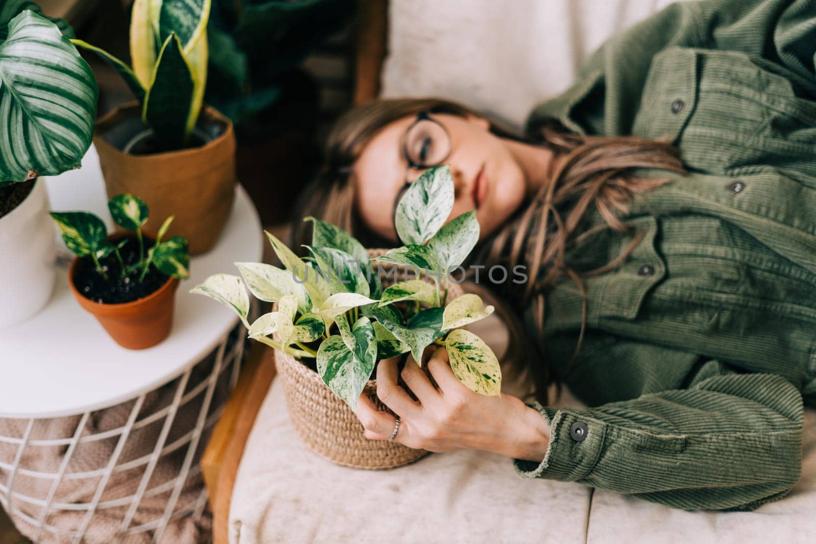 Young woman lying and sleeping and relaxing on the couch and a lot of plant . Cozy home and urban jungle concept